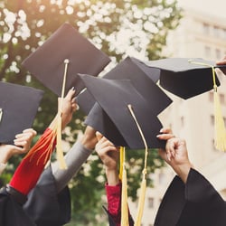 Graduation caps are held in the air by graduates.