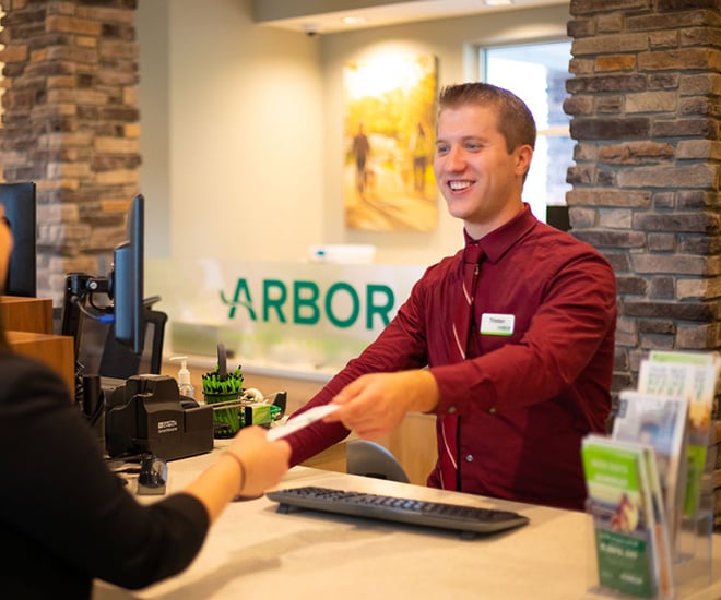 Arbor bank teller smiling while handing a customer their deposit slip.