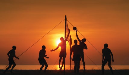 A group playing beach volleyball in the sunset.