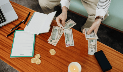 A person counts money on a coffee table, with a planner and notebook laid to the side.