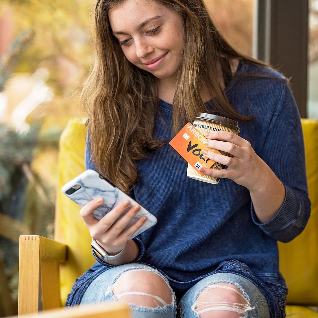 Student looking at phone, holding coffee and volt card